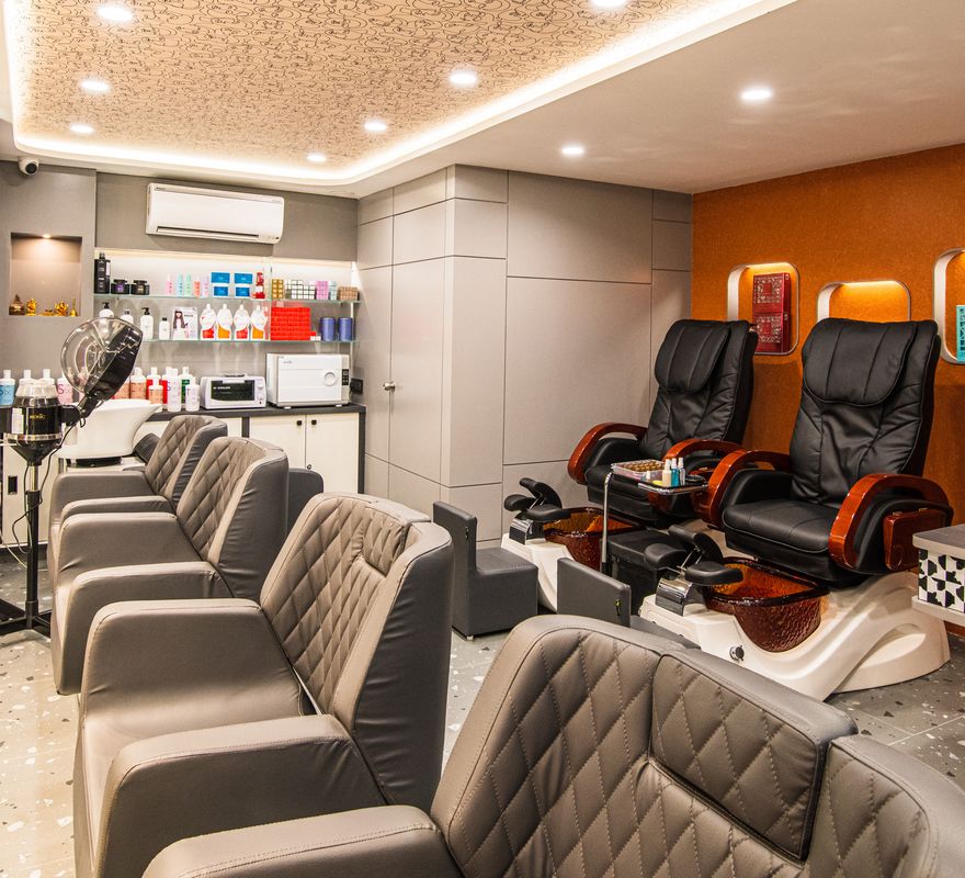 The nail lounge at Ftry Salon: two pedicure chairs against an orange wall beside a manicure table.